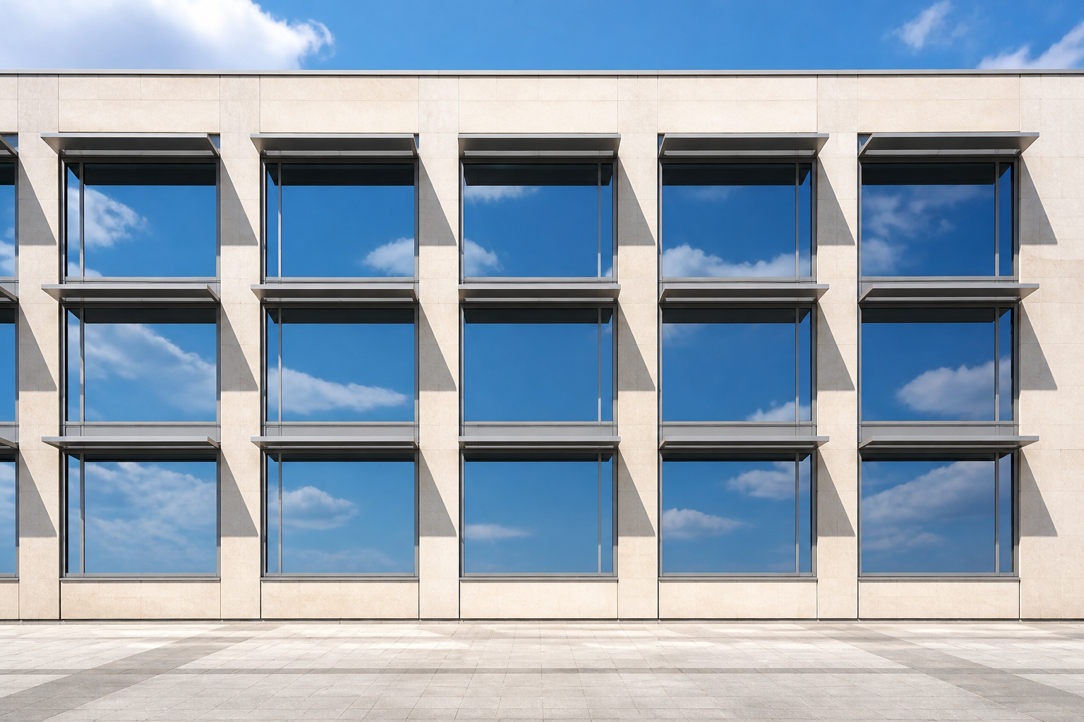 Exterior midday view of a modern building facade with an array of large fixed aluminum glass picture windows, slim horizontal external shading fins above each unit casting sharp shadows, pale stone cladding, glass reflecting sky and cloud, no people, no hardware close-up